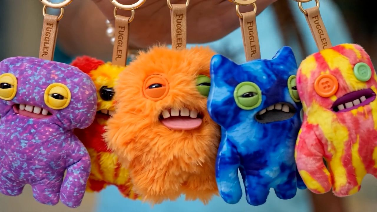 A hand holding a row of Fuggler plush keychains